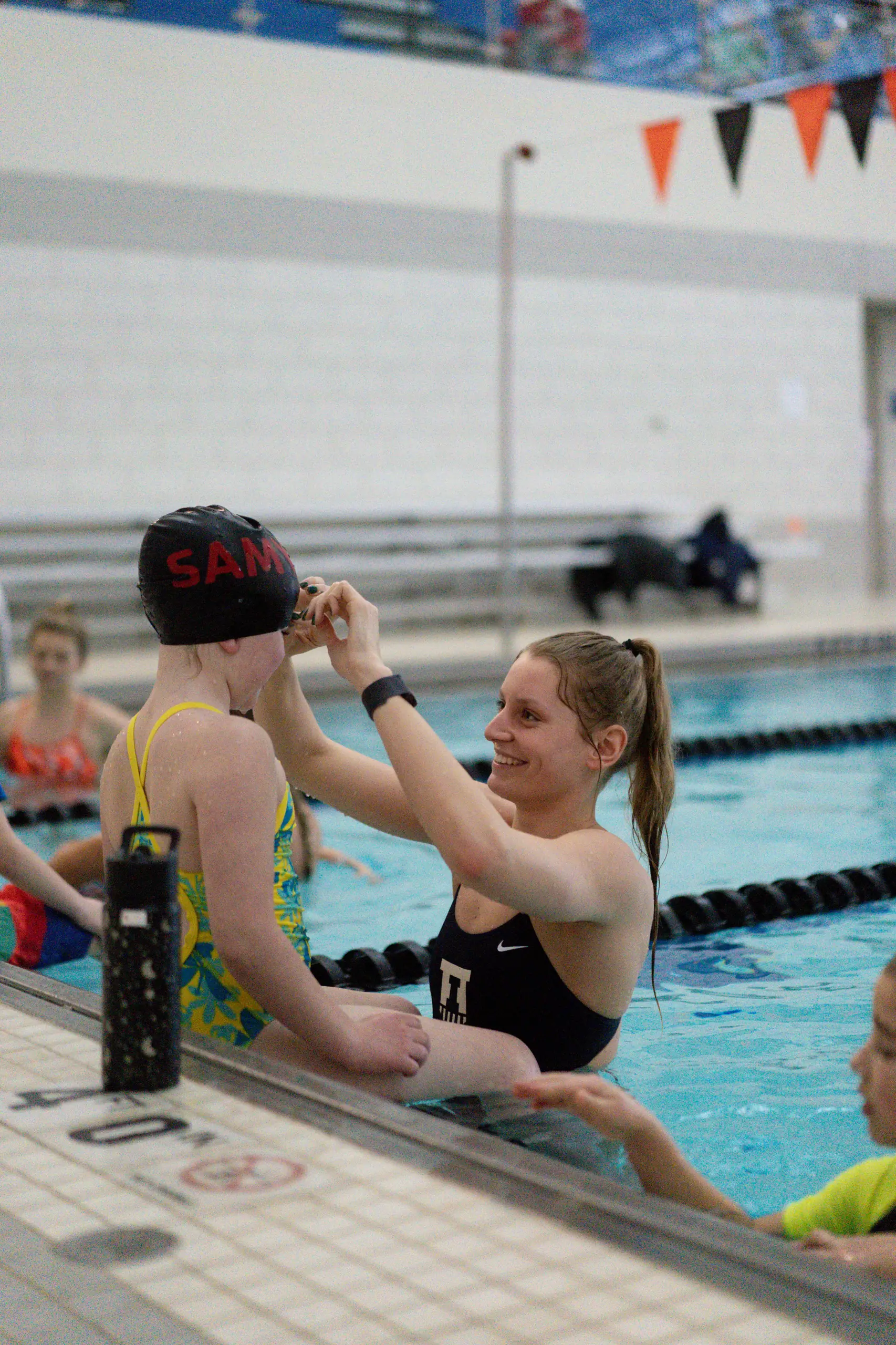 Sydney, a University of Illinois swimmer, helping a young camper with a swim cap poolside