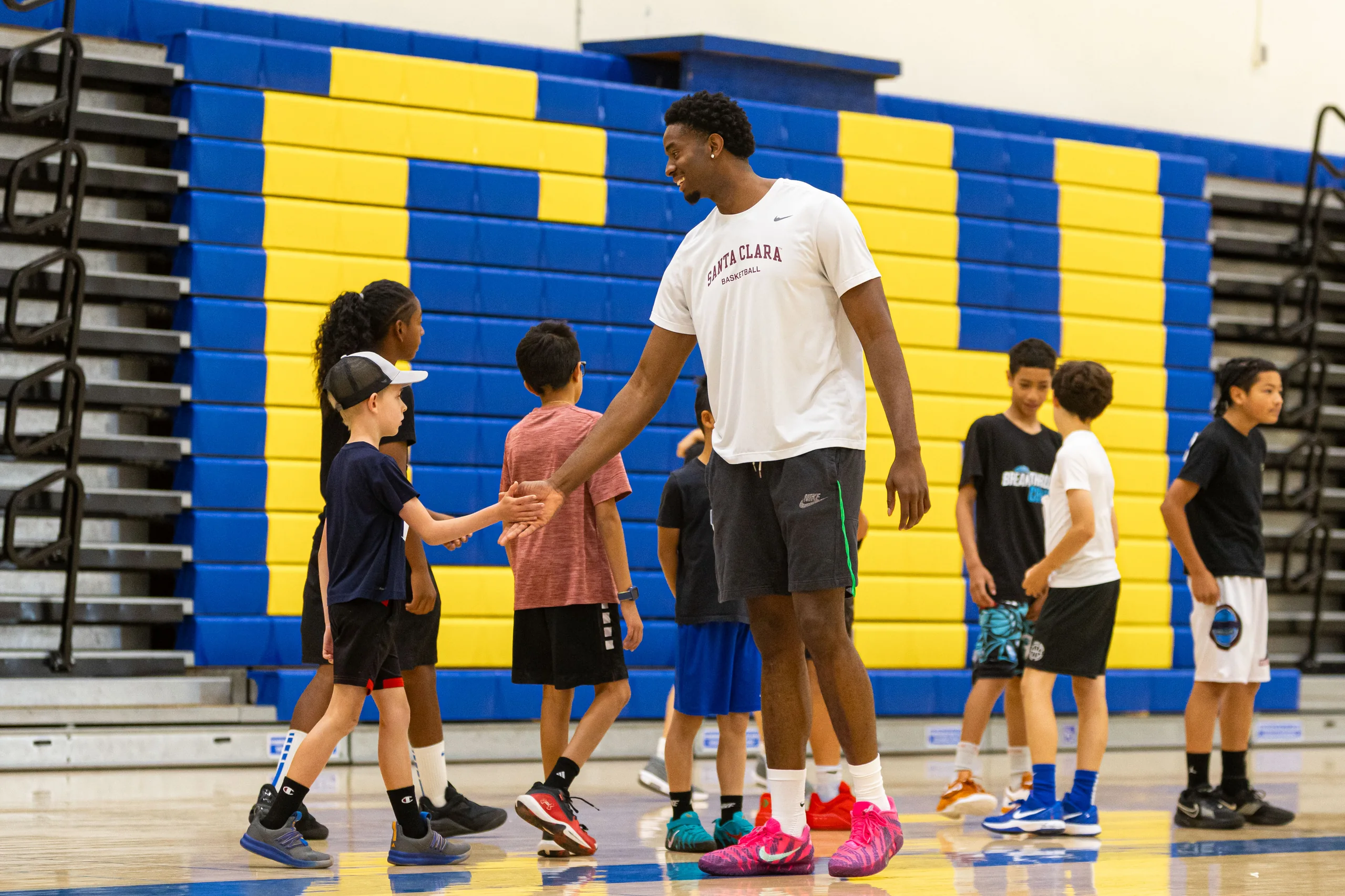 A college basketball player high-fiving a young camper at a Top Tier camp