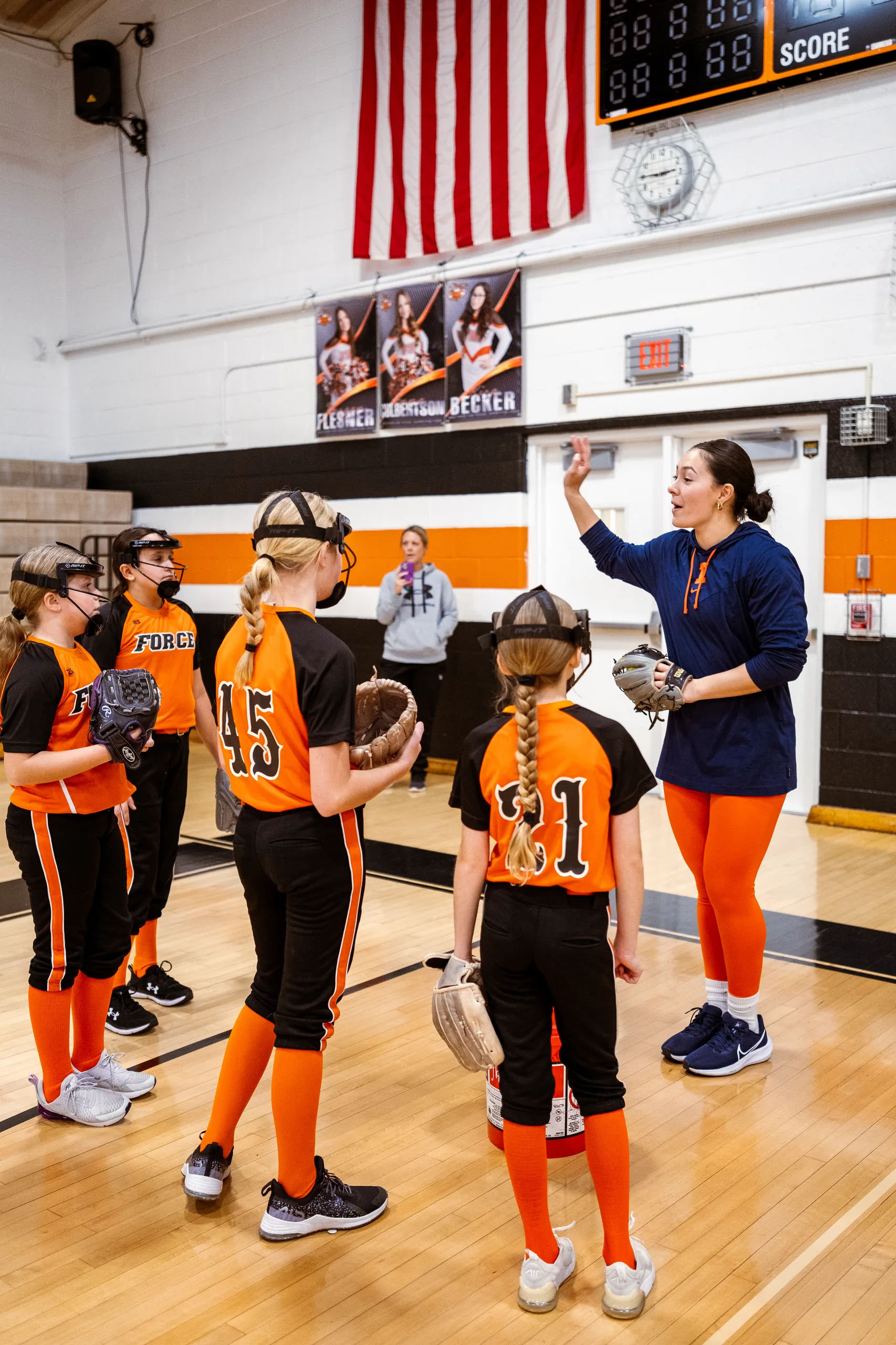 A college-athlete coach instructing young softball players in a gym