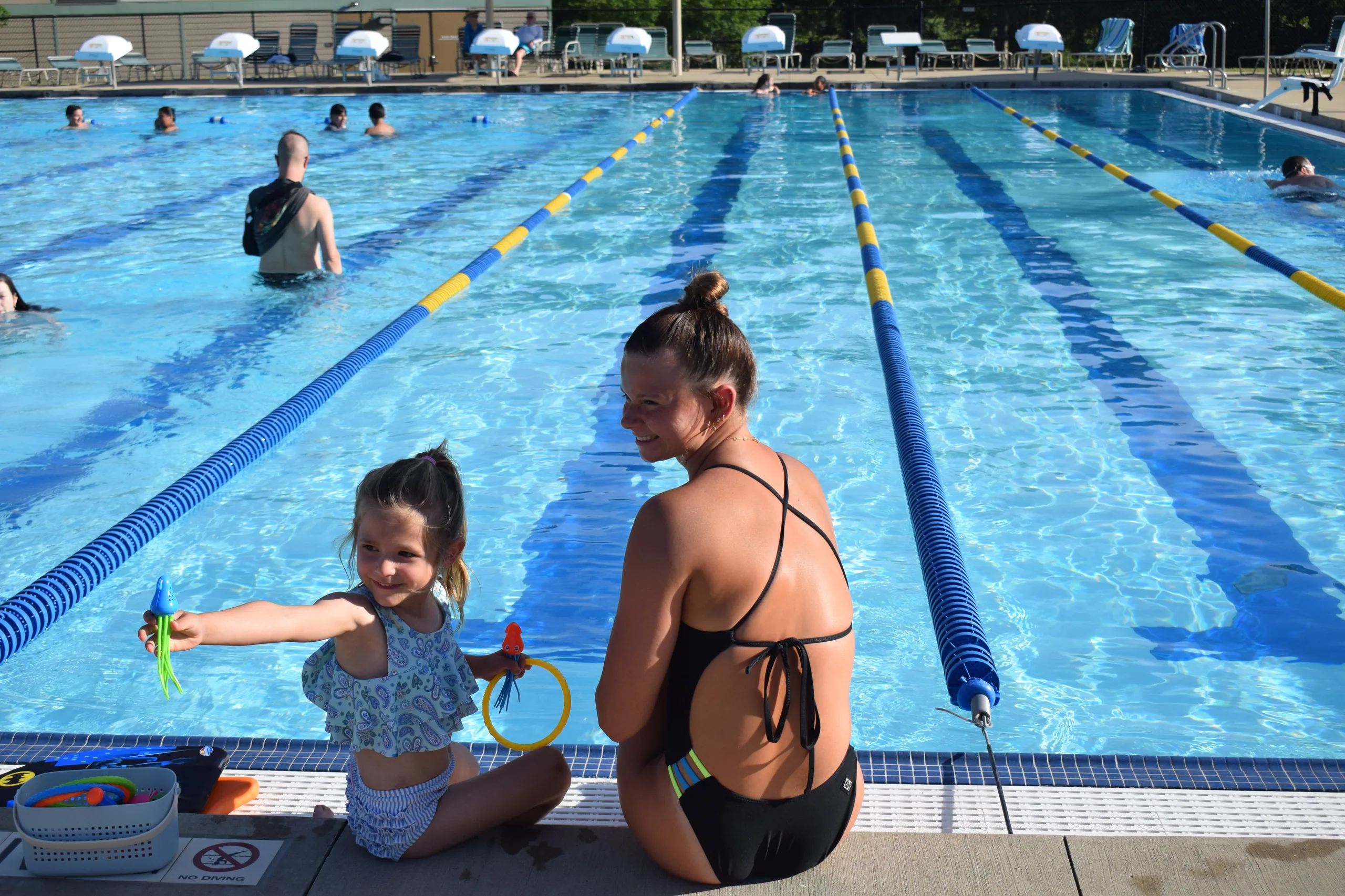 A college-athlete swim coach sitting poolside with a young camper