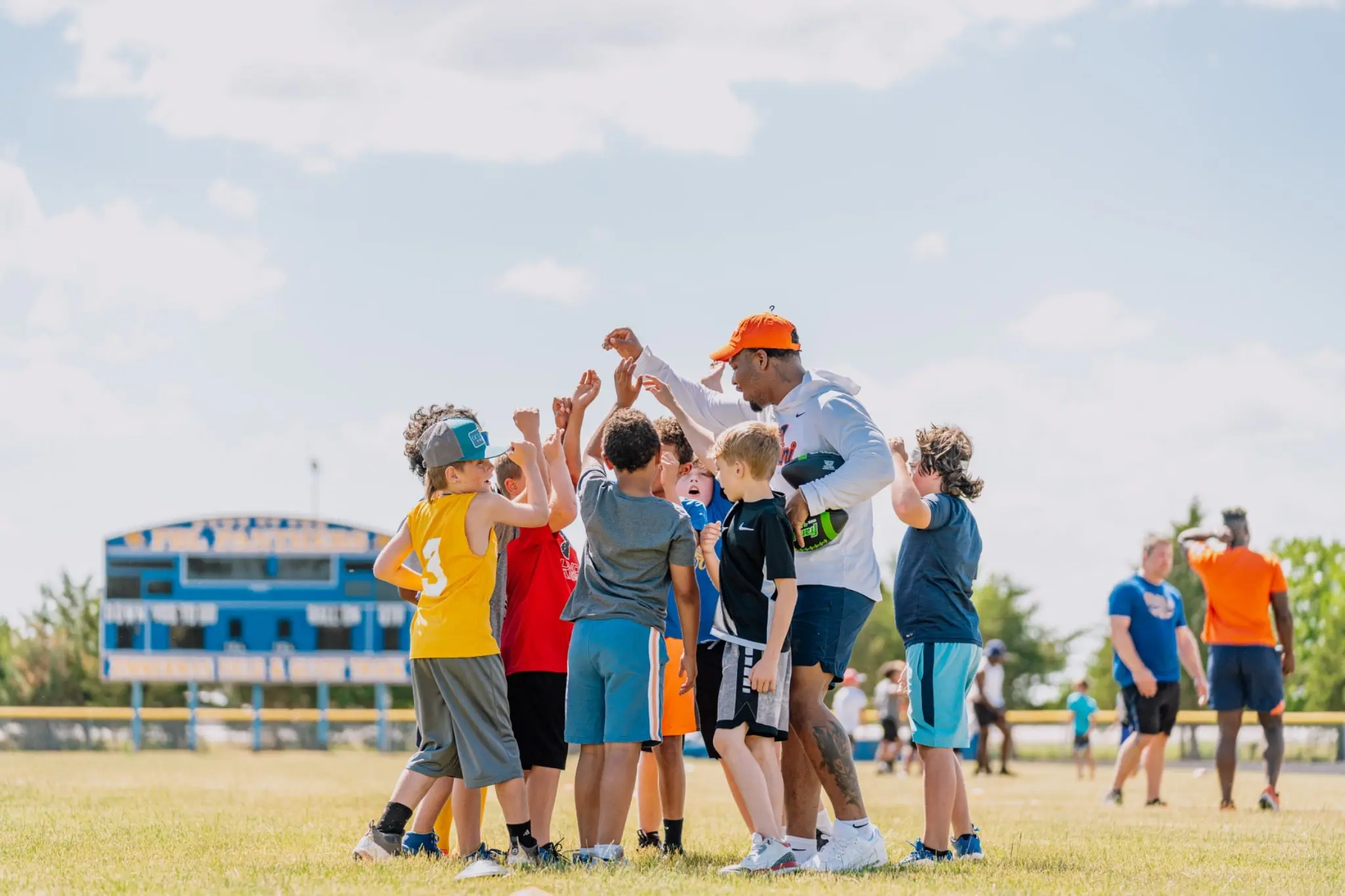 A college coach high-fiving a huddle of youth football campers on a field